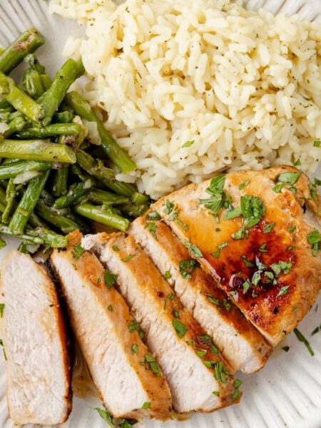 Sliced pork chop on a plate with rice and asparagus as sides.