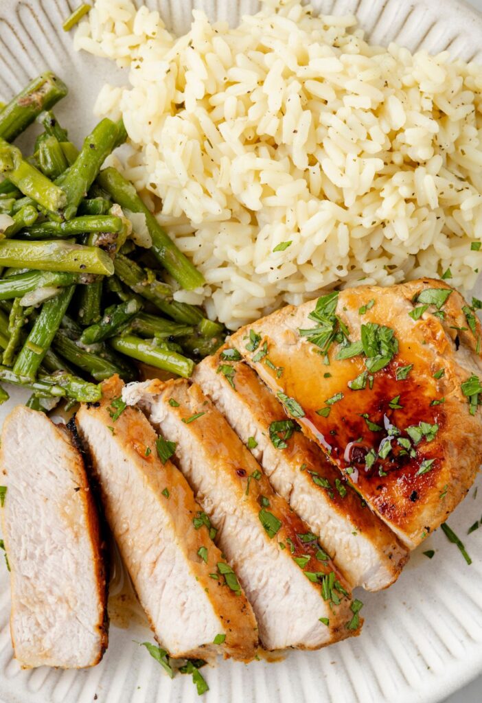 Sliced pork chop on a plate with rice and asparagus as sides. 