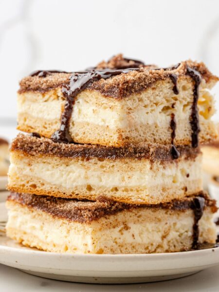 A stack of cheesecake bars with churro ingredients and chocolate sauce over top