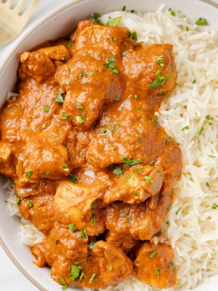 A serving bowl of rice with chicken tikka masala and sauce on it.