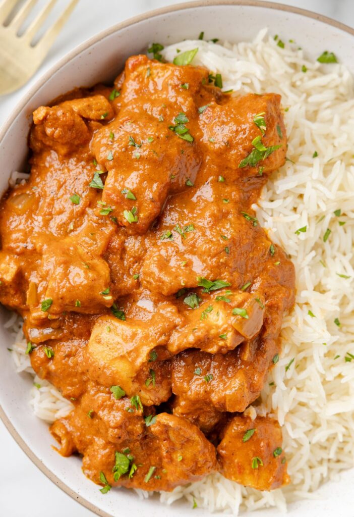 A serving bowl of rice with chicken tikka masala and sauce on it. 