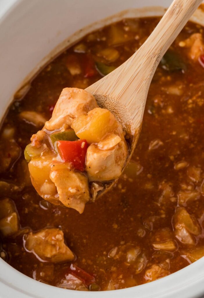 Pineapple Hawaiian chicken inside the crock pot with a serving spoon with some on it. 