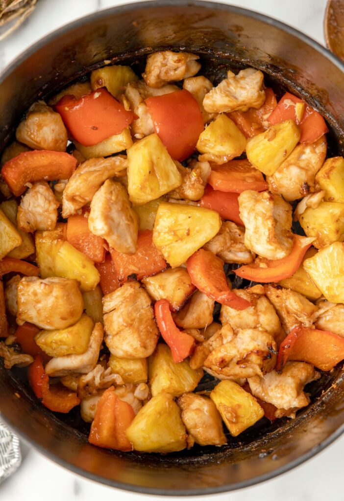 Air fryer basket with cooked pineapple chicken inside of it.