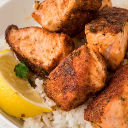 A bowl of rice with salmon bites and a lemon wedge.