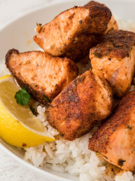 A bowl of rice with salmon bites and a lemon wedge.