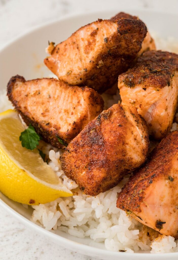A bowl of rice with salmon bites and a lemon wedge. 