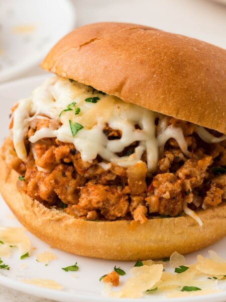 A sloppy Joe sandwich filled with meat filling on a white plate.