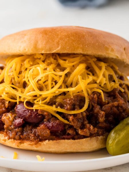 A sloppy Joe on a white plate with chili cheese mixture and cheese.