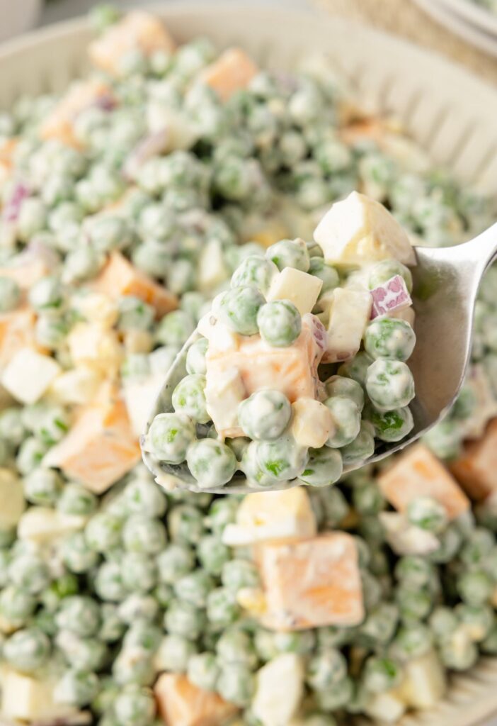 A spoon with a bite of the pea salad on it above the bowl of pea salad. 