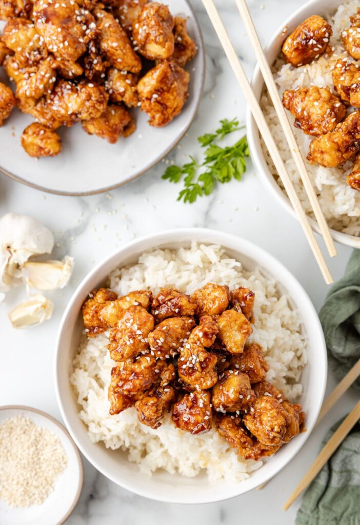 A bowl of crispy chicken with chopsticks and a plate of them next to the bowl. 