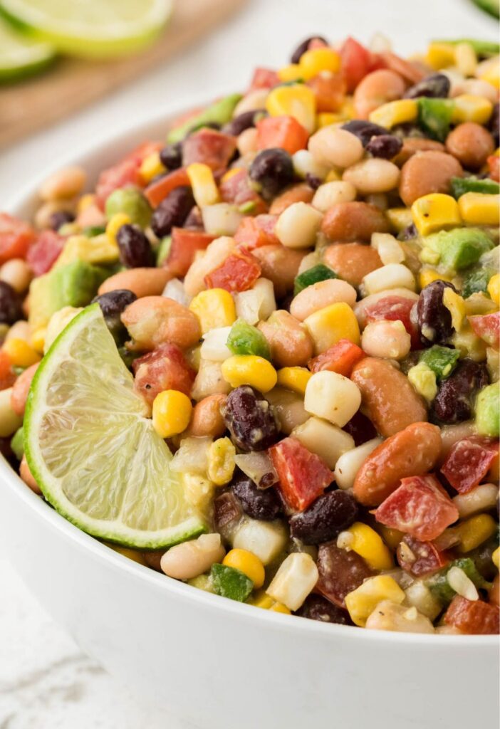 A white bowl of bean salsa with a lime wedge at the side.