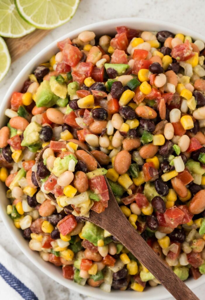 Overhead pic of a white bowl of bean salsa with a wooden serving spoon inside of it. 