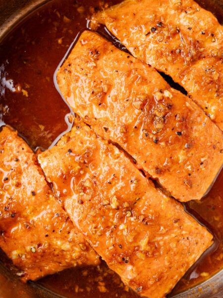 A stainless steel skillet with cooked and seared salmon inside of it.