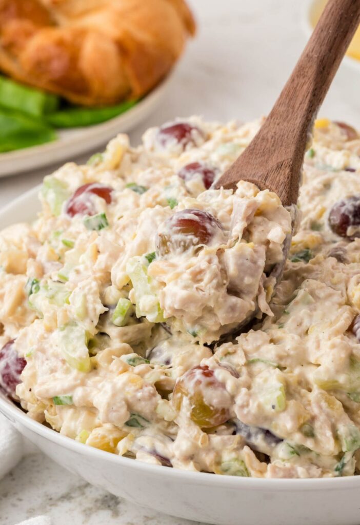 Serving bowl of chicken salad with a wooden serving spoon in it.