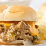 A sloppy Joe sandwich on a white plate with cheese oozing out of it.