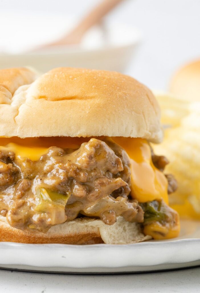 A sloppy Joe sandwich on a white plate with cheese oozing out of it. 