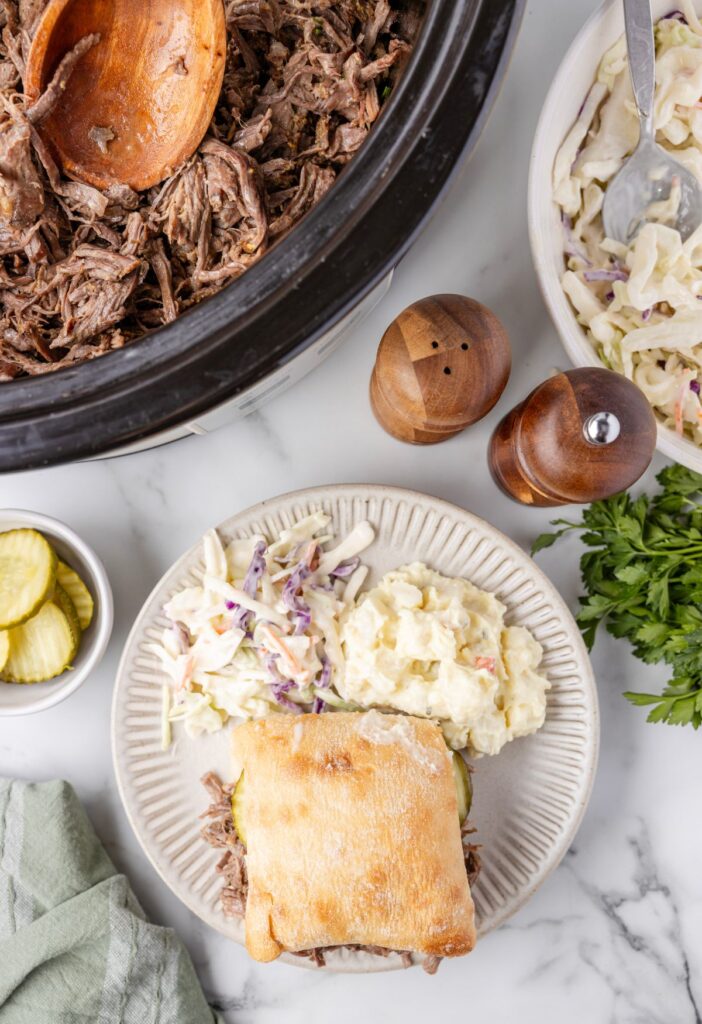 Overhead pic of the crockpot of shredded beef and a serving plate of a sandwich. 