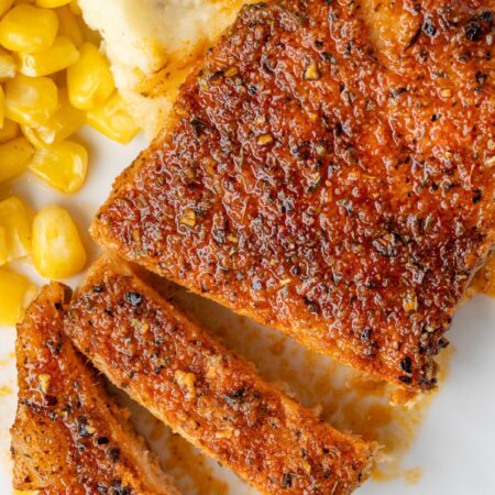 A white plate with mashed potatoes, corn, and pork chops on it that have been baked.