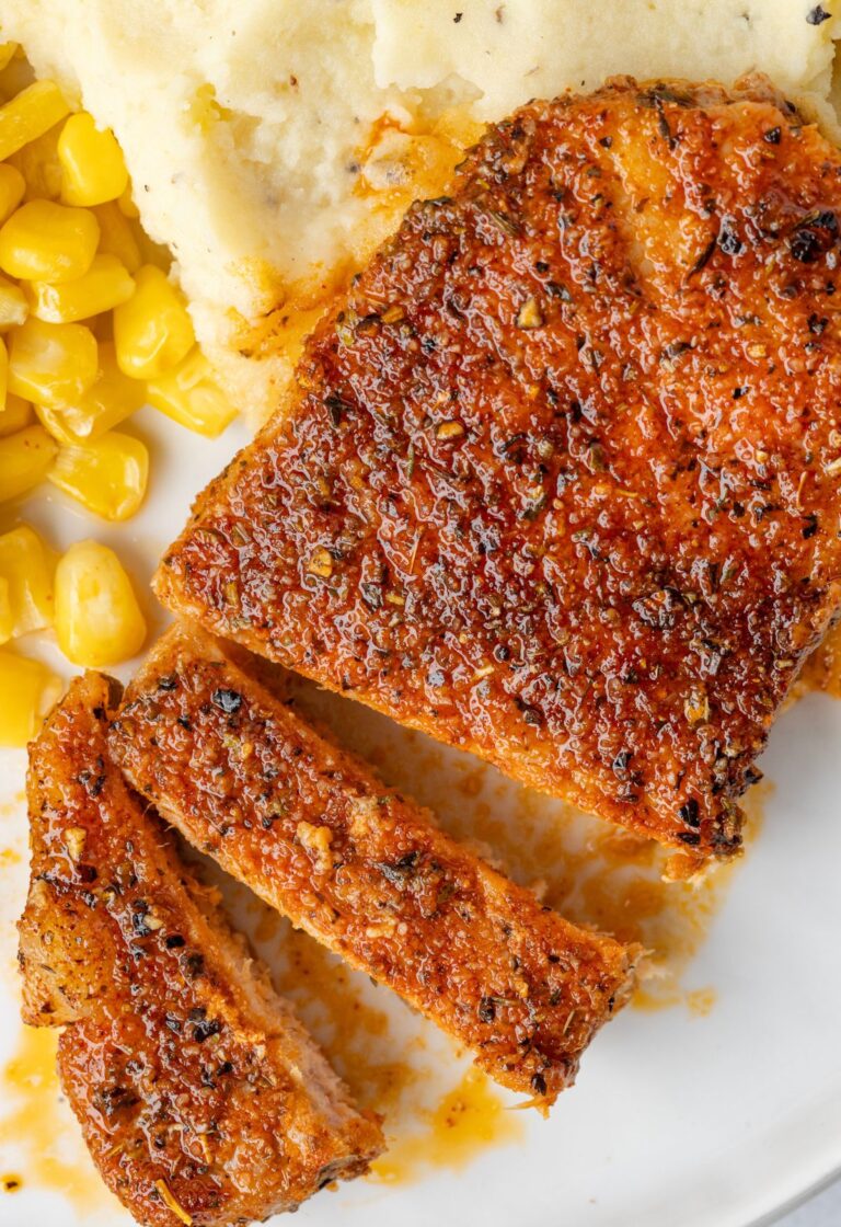A white plate with mashed potatoes, corn, and pork chops on it that have been baked.