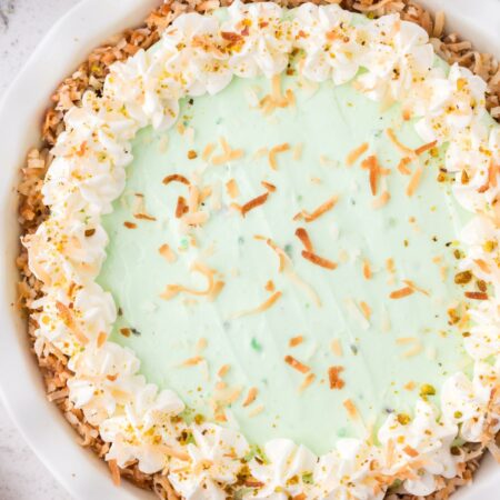A pistachio pudding pie inside a pie plate with whipped cream and coconut flakes on top.