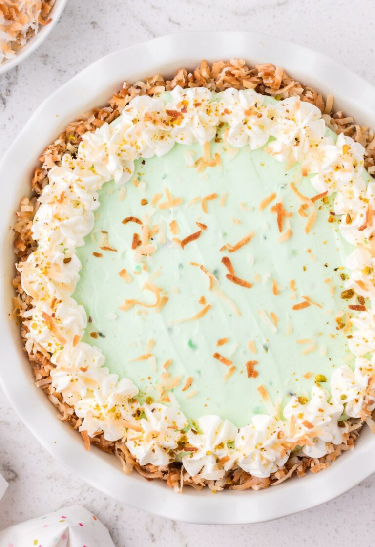 A pistachio pudding pie inside a pie plate with whipped cream and coconut flakes on top.