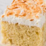 A slice of the tres leches cake on a white plate with toasted coconut on top.