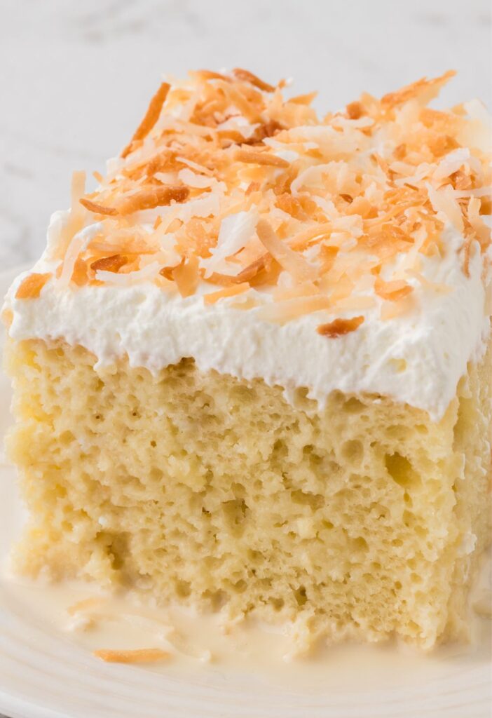A slice of the tres leches cake on a white plate with toasted coconut on top. 