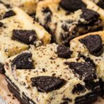 Side view of oreo cheesecake bars on a cooling rack on top of parchment paper.