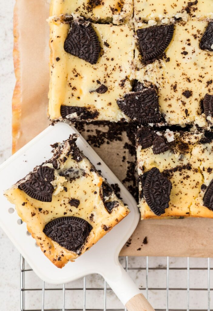 A serving spatula next to the cheesecake bars with a bar on it. 