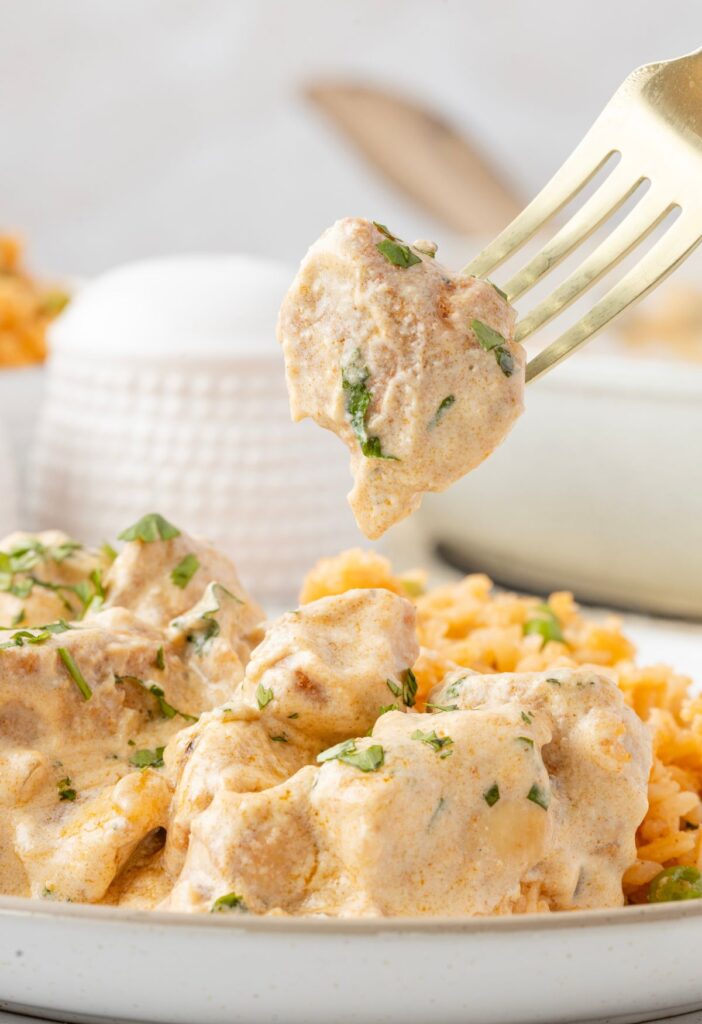 a fork with some pollo con crema on it above the plate of it