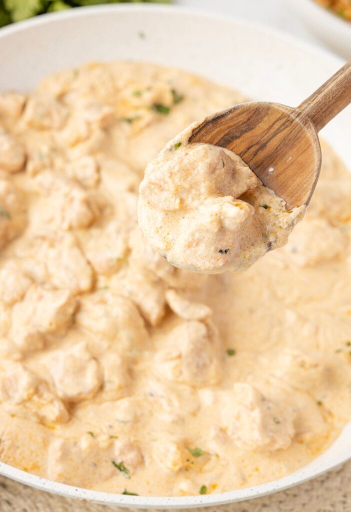A skillet pan with creamy chicken in it and a wooden serving spoon