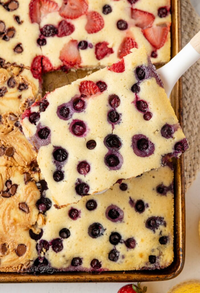 A spatula with a pancake on it over the sheet pan of pancakes below it