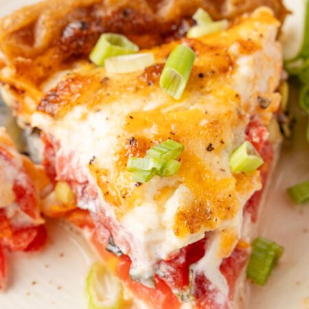 A slice of tomato pie on a white plate with a fork
