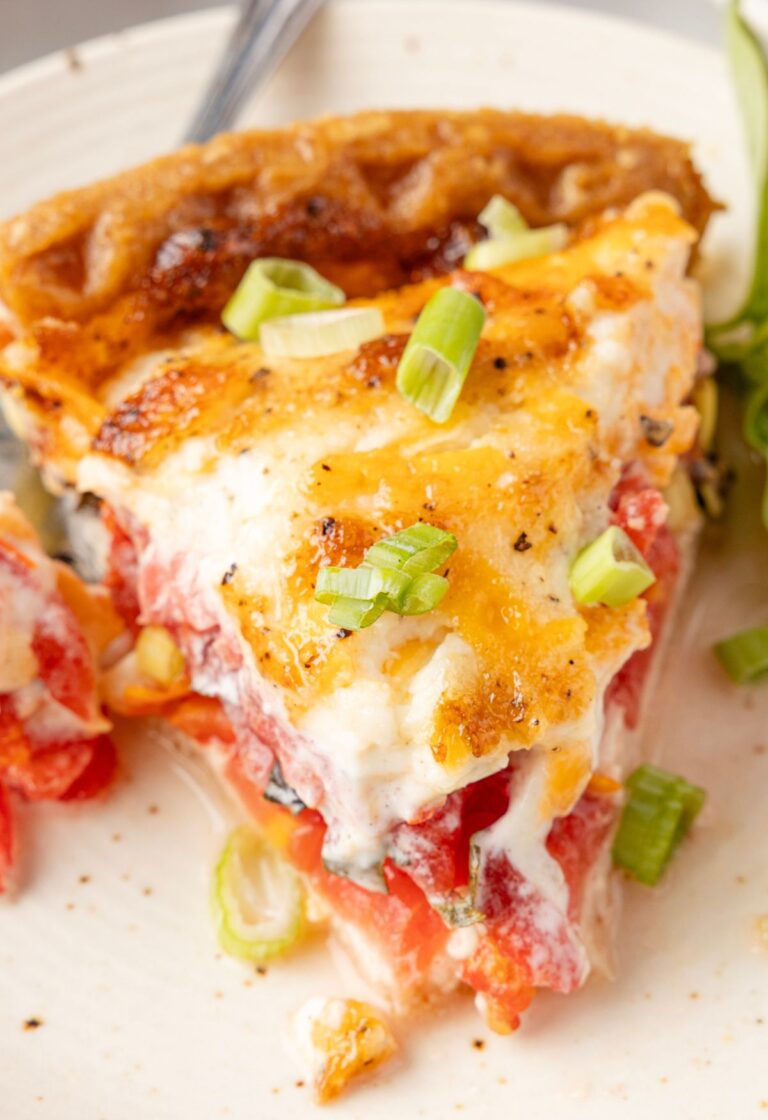 A slice of tomato pie on a white plate with a fork