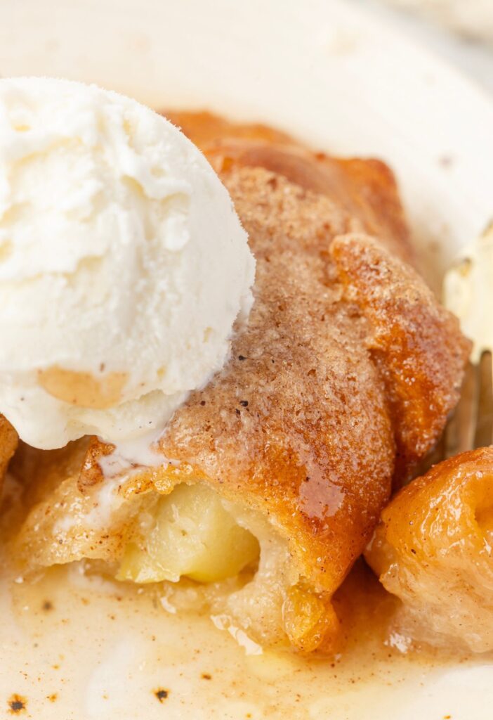 Apple dumpling topped with ice cream that's melted into it on a white serving plate. 