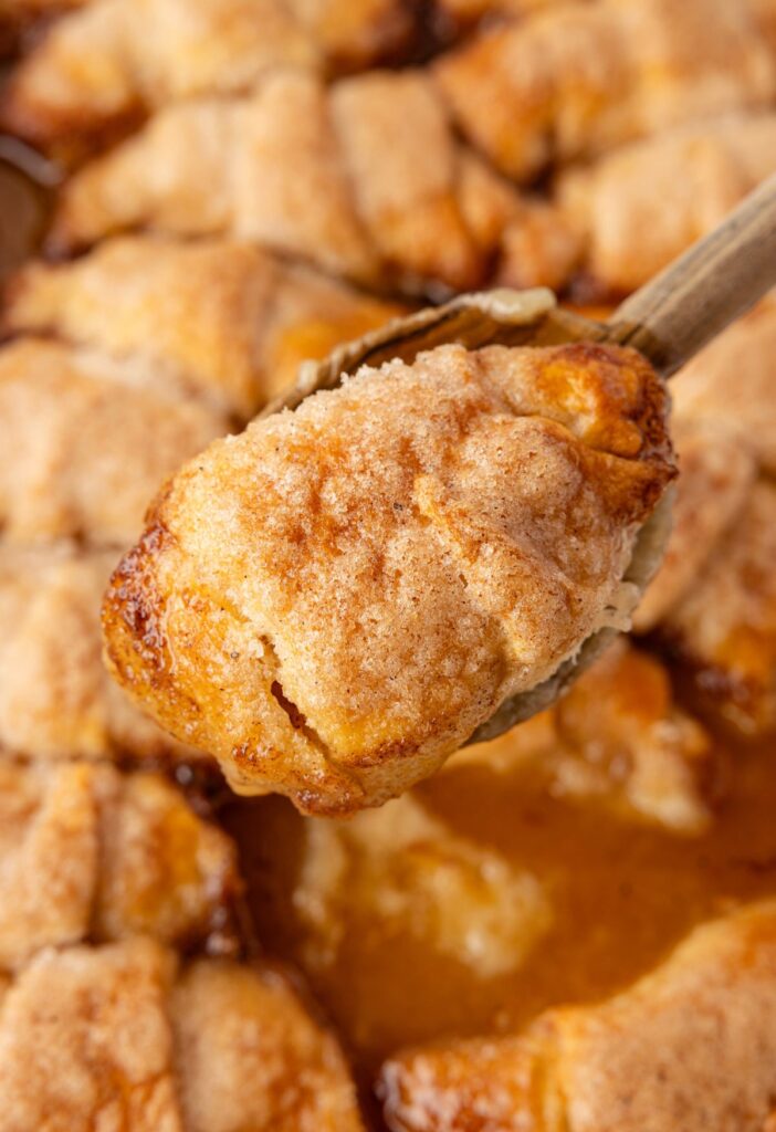 A wooden spoon holding an apple dumpling on it. 