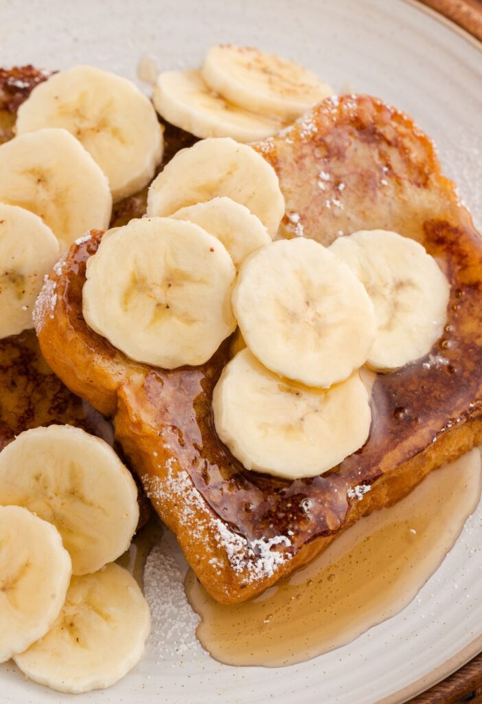 French toast on a white plate with banana slices and syrup.
