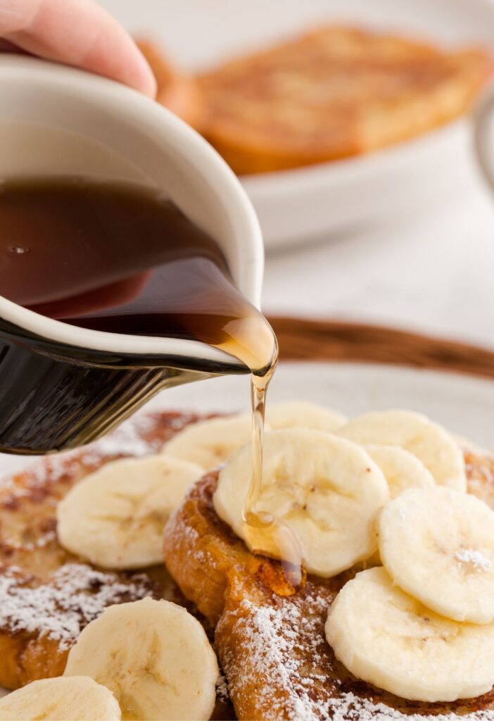 A cup pouring syrup out of it onto the French toast