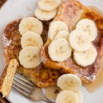 A fork with some French toast bread slices topped with syrup and banana slices.