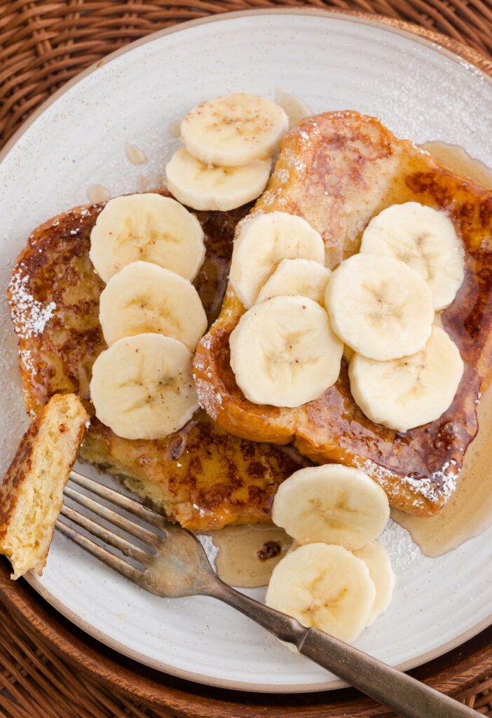 A fork with some French toast bread slices topped with syrup and banana slices. 