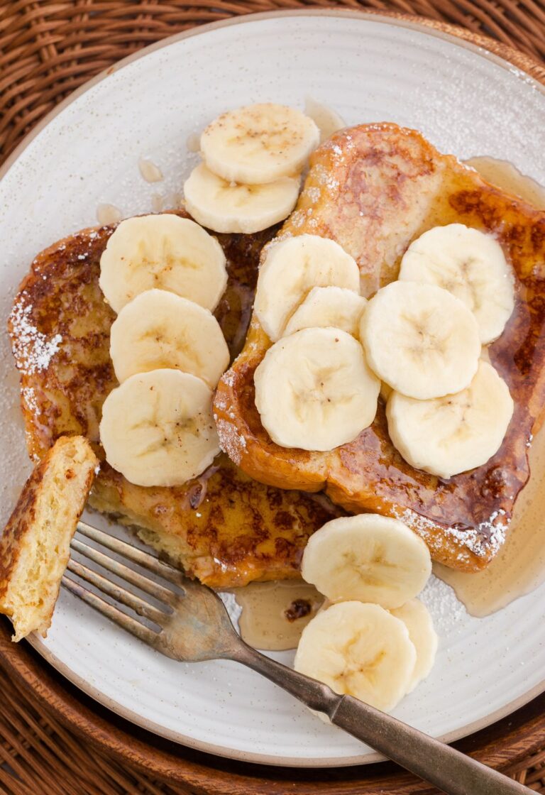 A fork with some French toast bread slices topped with syrup and banana slices.