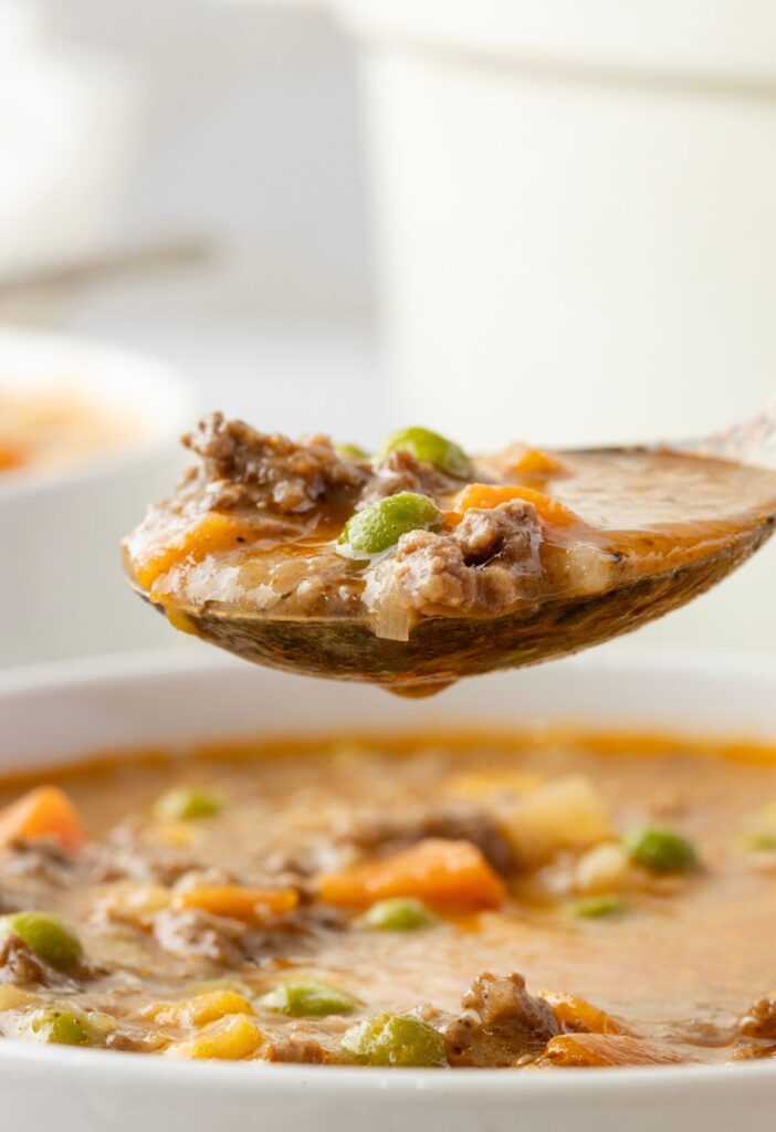 A side image of the spoon with soup on it above the serving bowl of cottage pie soup. 