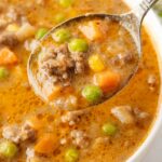 A white bowl with soup in it and a spoon with some soup on it.