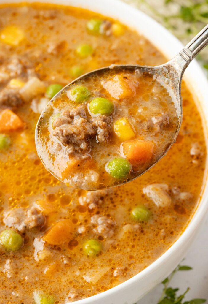 A white bowl with soup in it and a spoon with some soup on it. 