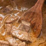 A wooden spoon with some steak bites on it from the crockpot.