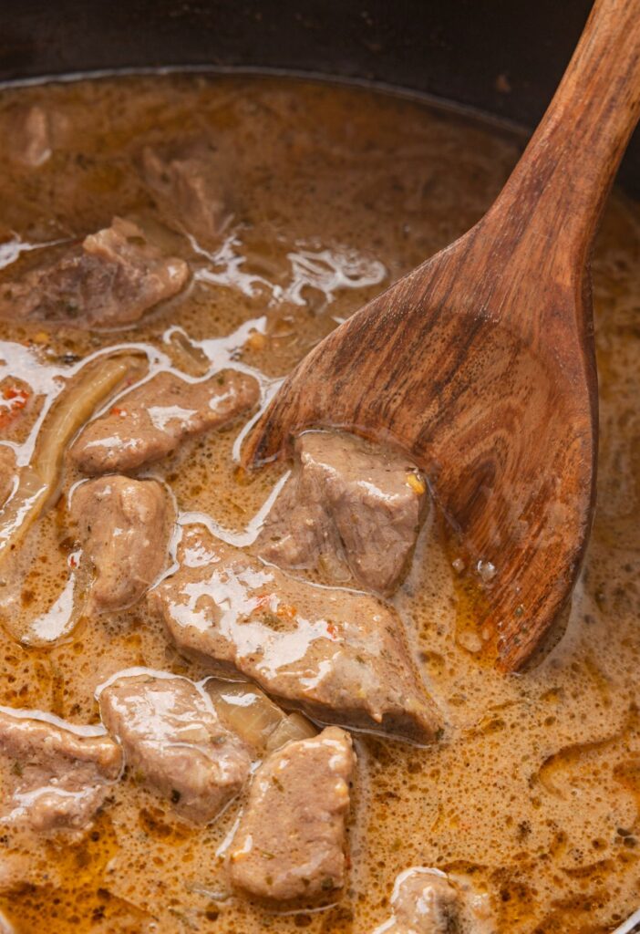 A wooden spoon with some steak bites on it from the crockpot. 
