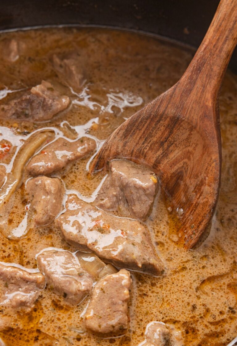 A wooden spoon with some steak bites on it from the crockpot.