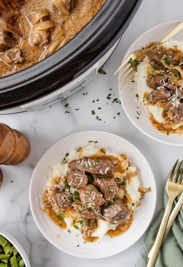 Overhead image of the crockpot with steak bites in it and a serving plate of it. 