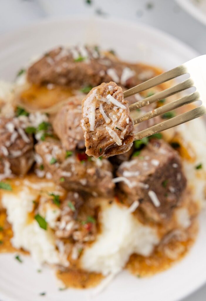 A fork with a steak bite on it above the serving plate. 