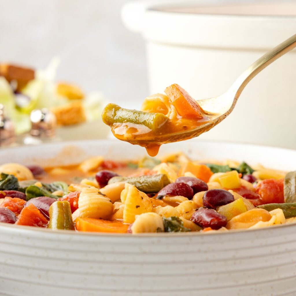 Side view of the bowl of soup with a spoon above the bowl with soup on it.